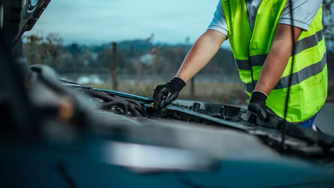 car broken down on the side of the road and mechanic is looking into it. 