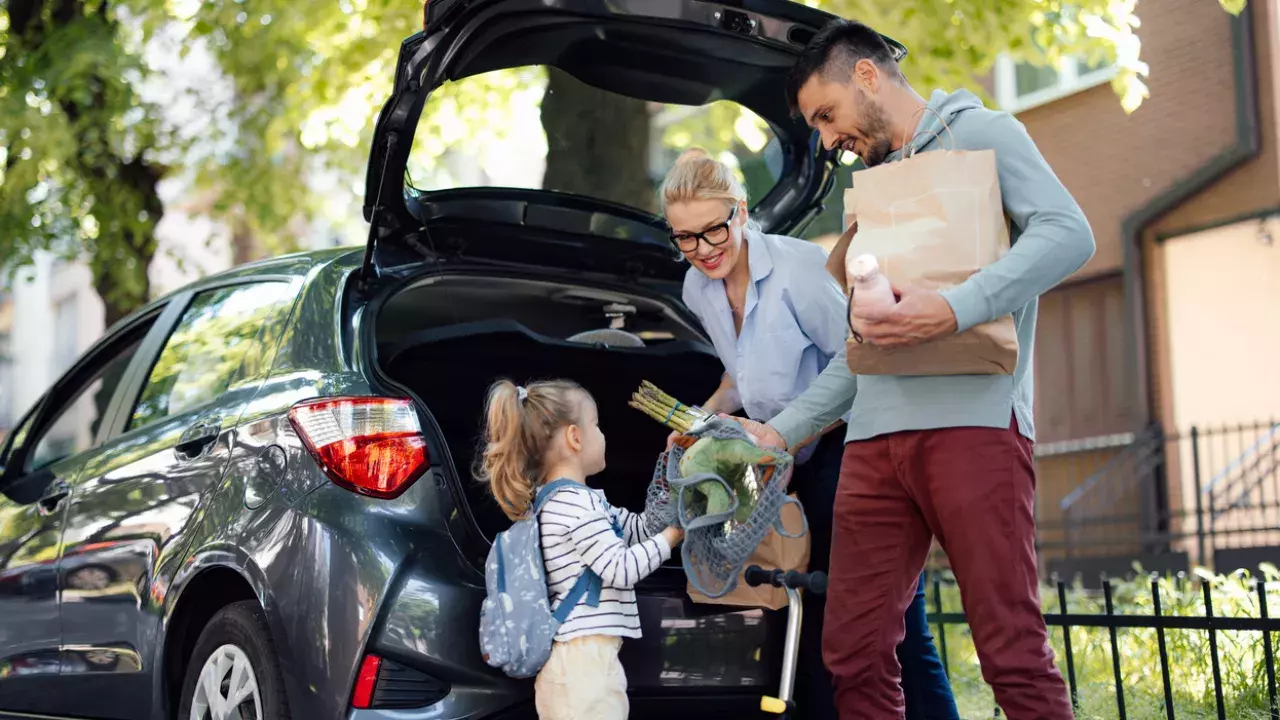 couple with their daughter standing behind the car with the boot open. 