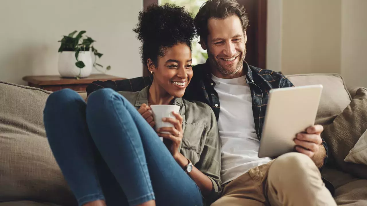 Husband and wife together on couch at home reviewing documents on a tablet screen