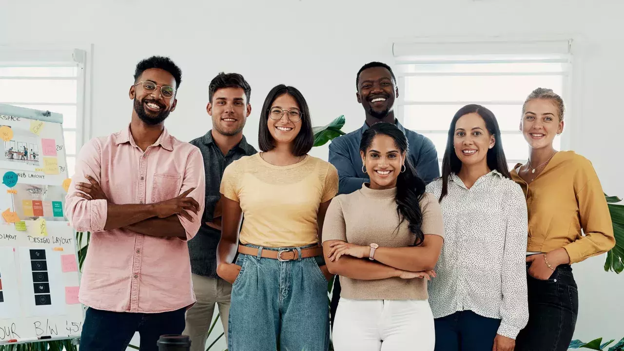 Seven business professionals smiling at the camera in an office setting 