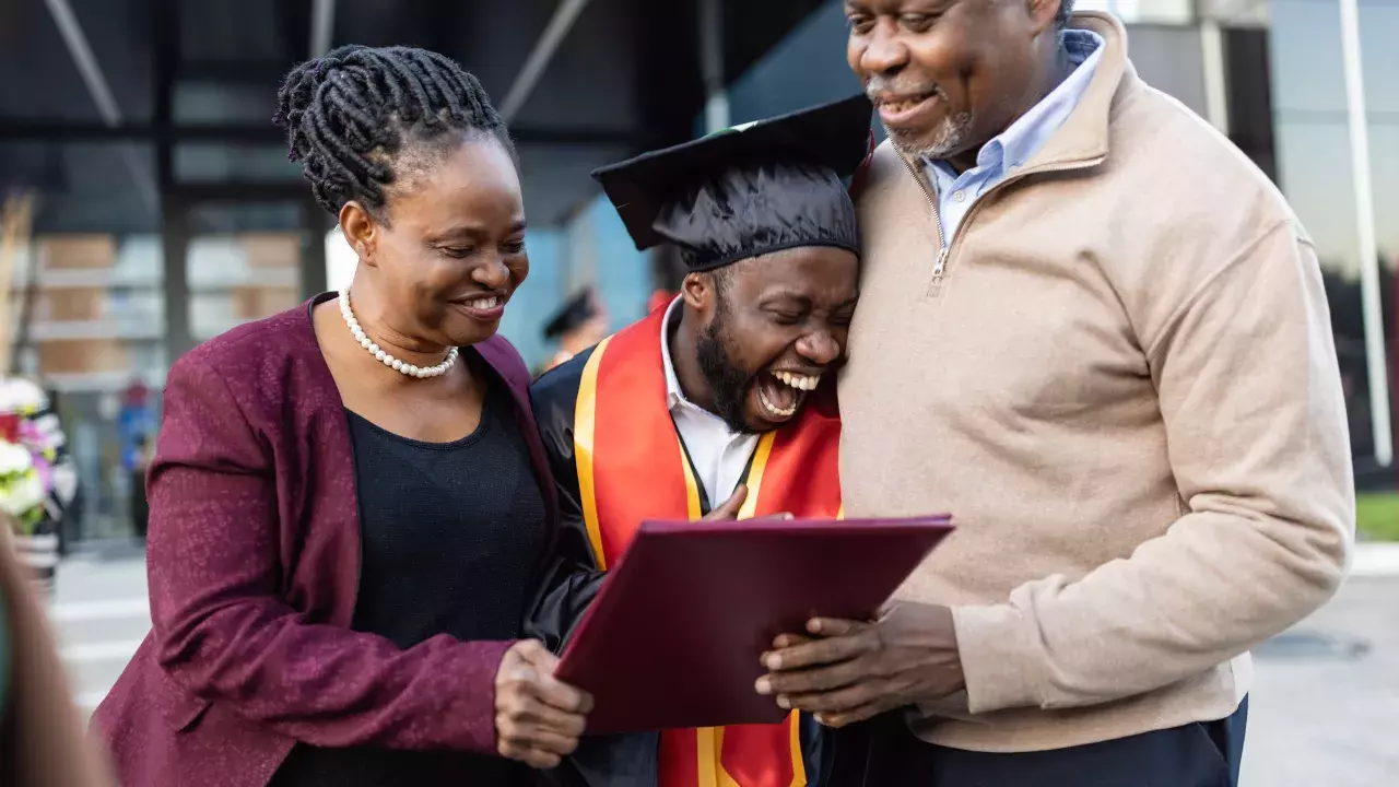 Mother and father hugging their graduating son holding a diploma in celebration