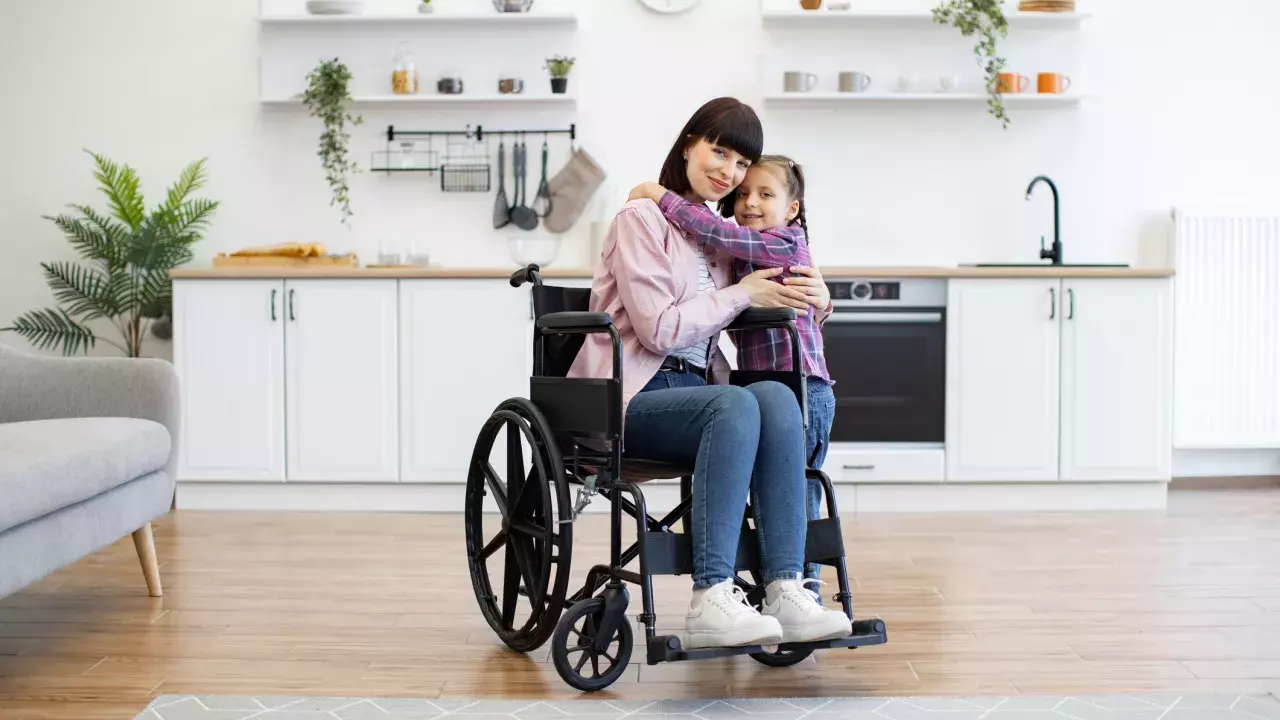 Mother sitting in a wheelchair hugging daughter at home