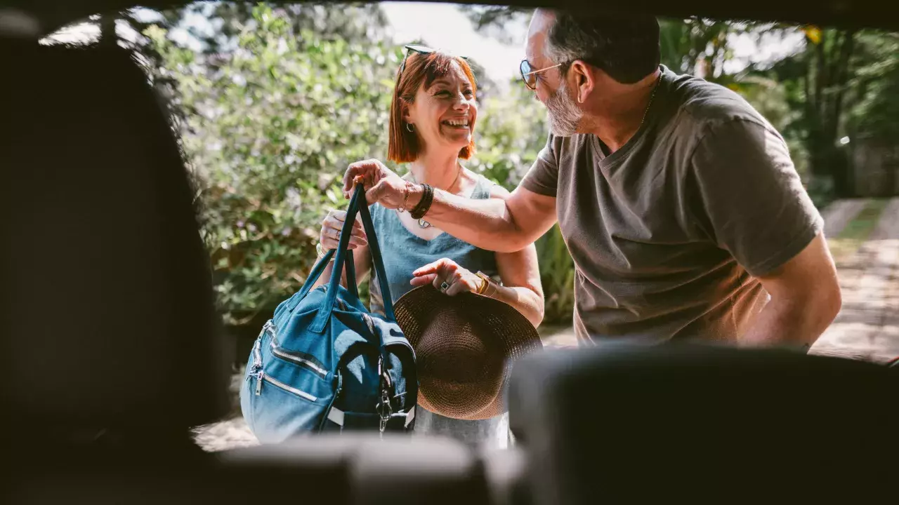 Smiling couple packing their luggage into the trunk of their car 