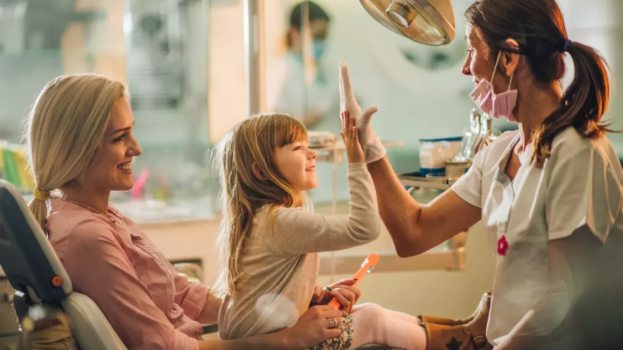 Mother and happy young girl hi-fiving dentist at dental checkup