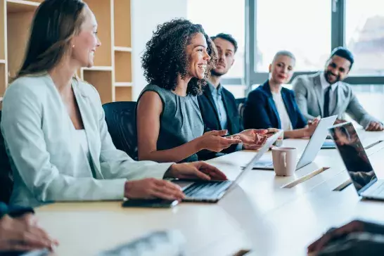 a group of 5 business people in a meeting discussing work, focusing on the middle woman who is speaking