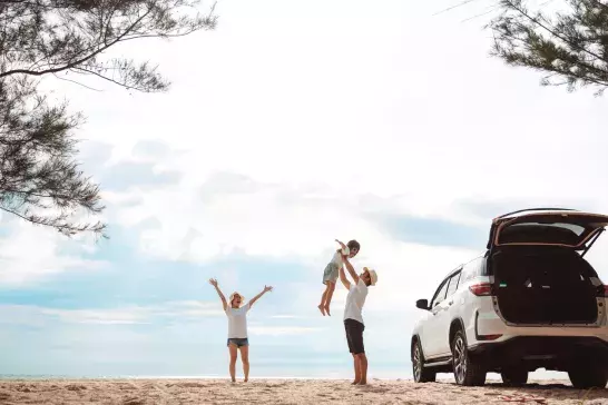 Family laughing together with their car parked on a beach