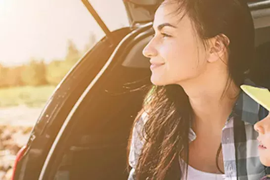 A mother and daughter sitting in an open hatchback vehicle looking into the distance