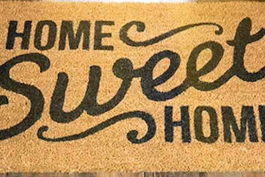 Image of a door mat saying Home Sweet Home surrounded by moving boxes