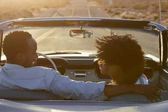 Rear view of couple on road trip in convertible at sunset