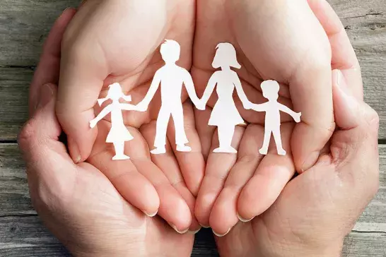 Hands holding a paper cutout of a family.