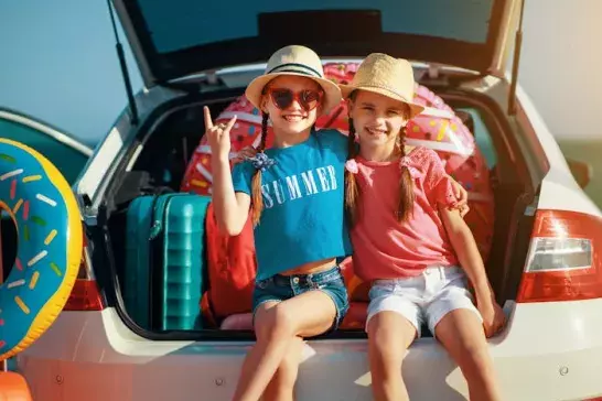 Two kids stting in open trunk of station wagon ready to go on a summer road trip