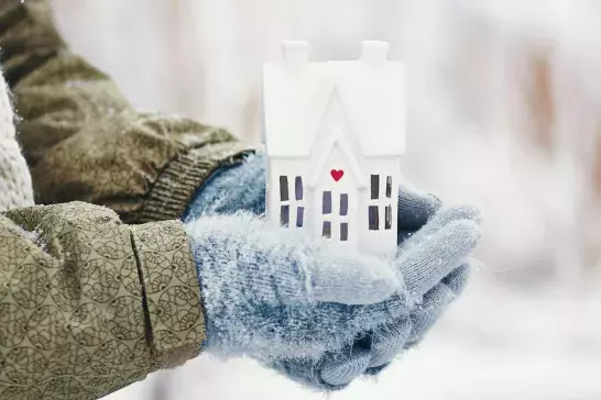 Female hands holding tiny house in snowy weather