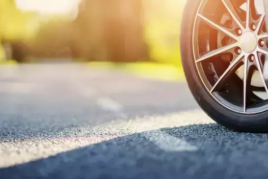 Front tire of blue car on asphalt road in summer