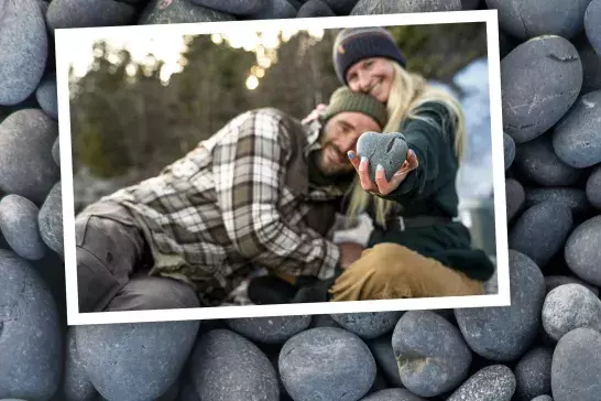 A couple are nestled together and the girl hold a heart shaped stone in hand