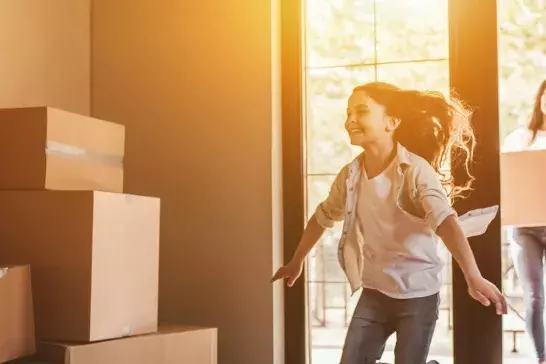 Family carrying moving boxes with girl running into new home