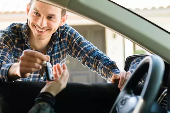 man passing keys to a woman through her car window