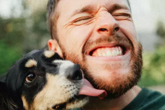 Man holding his dog and smiles as the dog licks his face