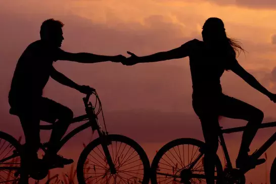 A couple rides bicycles at sunset.