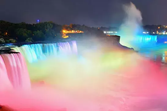 A picture of Niagra Falls  lit up in multiple colours at night