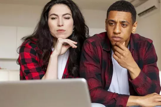 A man and woman thinking over a laptop screen