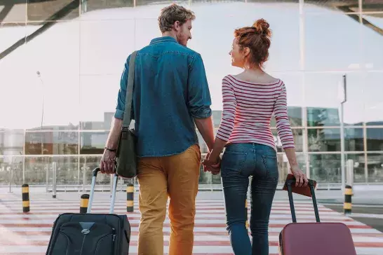 Young Couple walking with suitcases into airport leaving on vacation