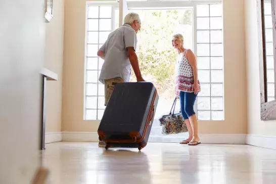 Senior Couple Standing By Front Door With Suitcase About To Leave For Vacation