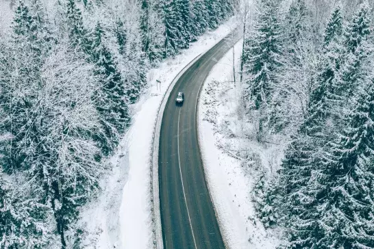 Aerial view of winter road with car and snow covered trees in the forest