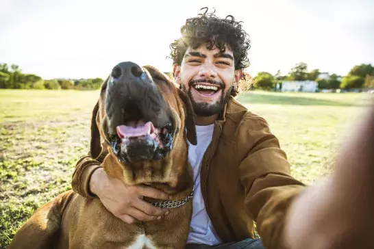 Young happy man taking selfie with his dog in a park - Smiling guy and puppy having fun together outdoor - Friendship and love between humans and animals concept