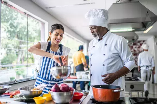 Student cooking and teacher helping in a cooking class