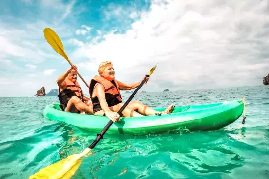 Happy retired couple enjoying travel moment paddling on kayak at Angthong marine park in Ko Samui in Thailand - Active elderly concept around world nature wonders - Bright vivid filtered tone