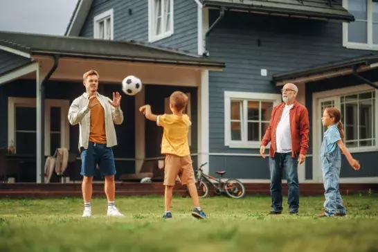 Family Spending Leisure Time Outside with Kids, Grandfather Playing with Ball with a Children. People Throwing the Ball Between Each Other, Having Fun on a Lawn in Their Front Yard.