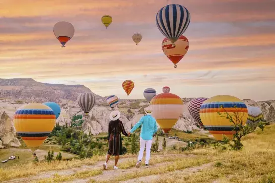 Cappadocia Turkey during sunrise, couple mid age men and woman on vacation in the hills of Goreme Capadocia Turkey, men and woman looking sunrsise with hot air balloons in Cappadocia