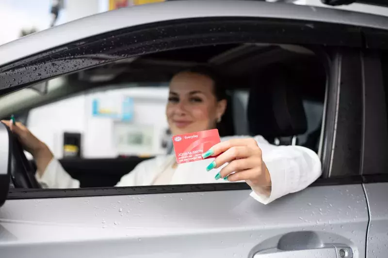 Female driver holds Everyday Membership card out window of vehicle at a Shell station