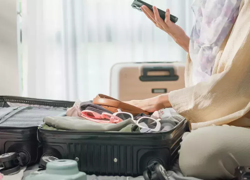 Woman packing a suitcase while looking at her phone