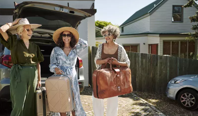 female friends smiling while standing at the trunk of their car full of luggage in a driveway