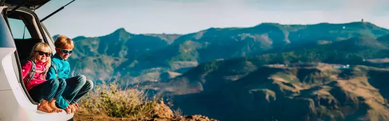 Happy boy and girl travel by car in mountains