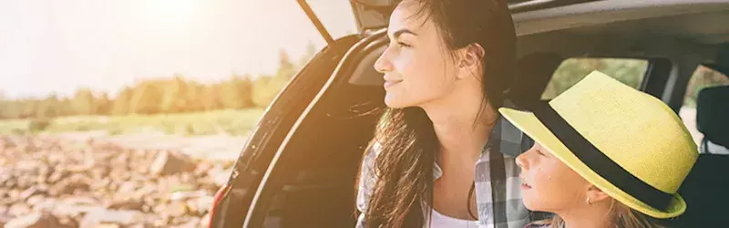 A mother and daughter sitting in an open hatchback vehicle looking into the distance