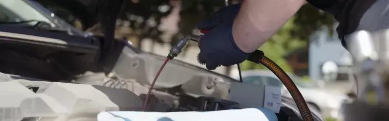 Hands under the hood of a vehicle doing an oil change