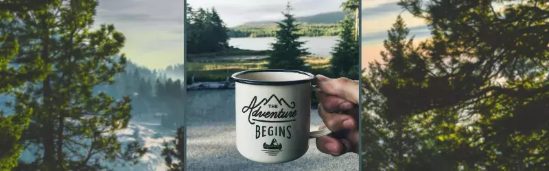 An enamel cup with print is held by a hand against the backdrop of a forest.