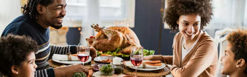 Happy black family talking during Thanksgiving meal at dining table.