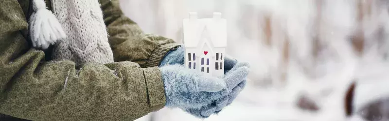 Female hands holding tiny house in snowy weather