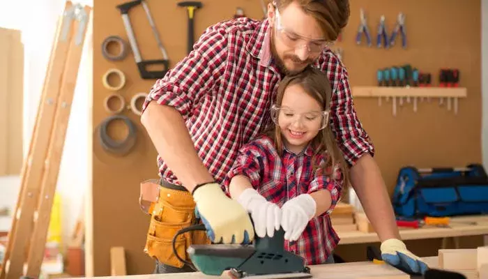 Dad sands piece of wood in workshop with daughter