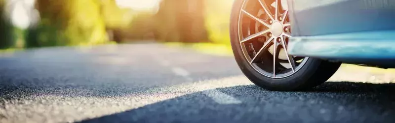 Front tire of blue car on asphalt road in summer