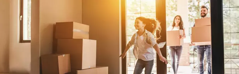 Family carrying moving boxes with girl running into new home