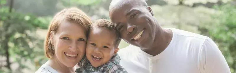 A mixed race family of three smiling at the camera