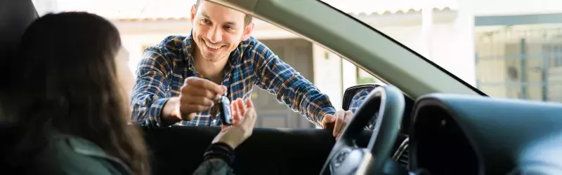 man passing keys to a woman through her car window