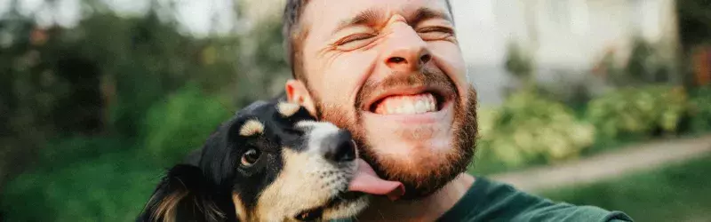 Man holding his dog and smiles as the dog licks his face