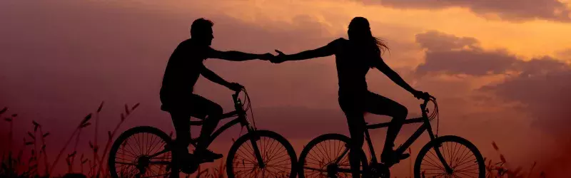 A couple rides bicycles at sunset.