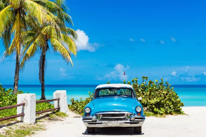 American blue classic car with a white roof parked under palms direct on the beach in Varadero Cuba - Serie Cuba Reportage