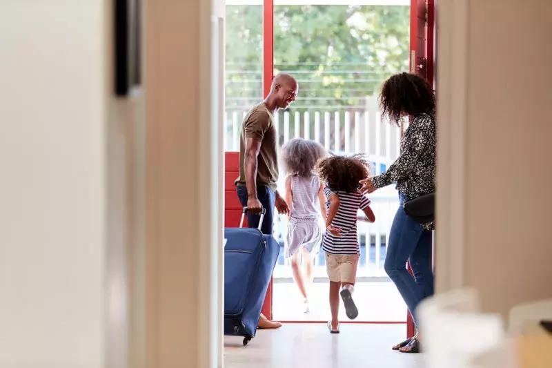 Family Standing By Front Door With Suitcase About To Leave For Vacation